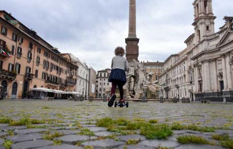 4. Esma Cakir / Agenzia DHA Roma, 18 aprile 2020. In una Piazza Navona deserta, con l’erba che cresce tra i sampietrini, una bambina corre in monopattino dopo la decisione del governo di permettere brevi uscite per fare esercizio fisico.